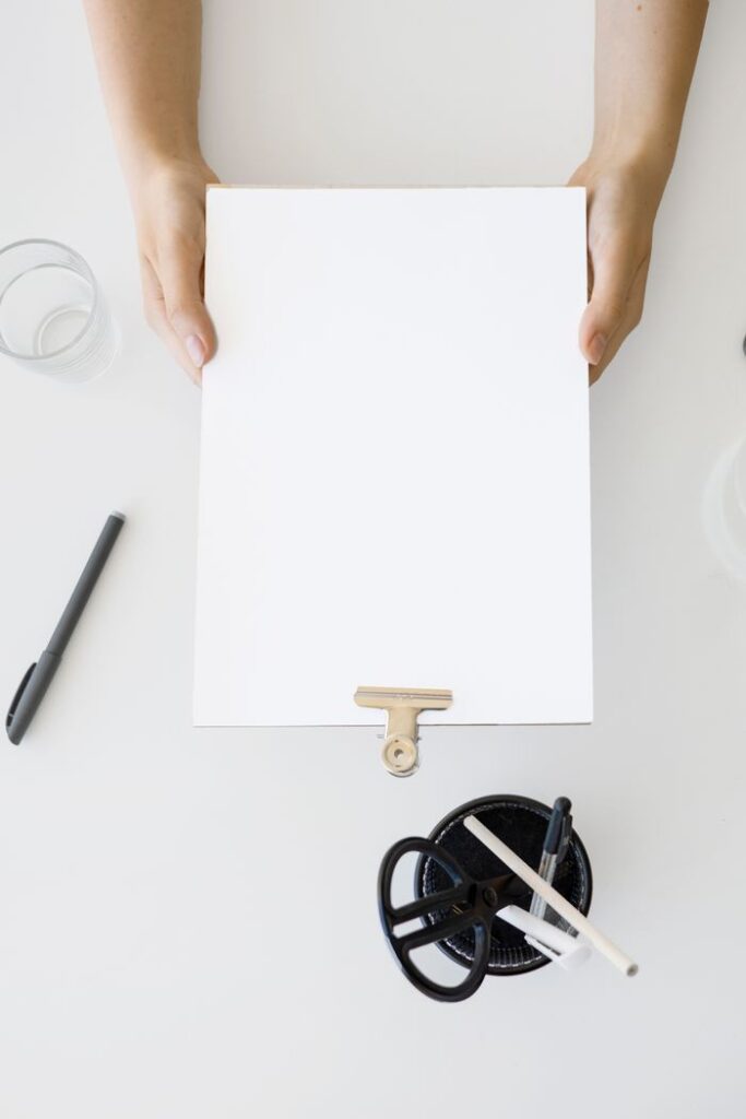 The Art of Drawing Readers In: Your attractive post title goes here Top view of hands holding a blank clipboard surrounded by office items for a mockup or concept design.